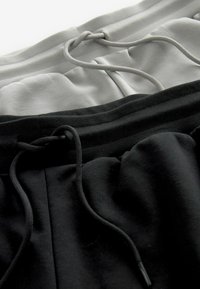 Deux paires de jogging en gris et noir, dotées de ceintures élastiques avec cordons de serrage et d'une texture de tissu douce et lisse.