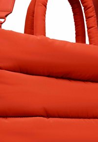 Rote gepolsterte Handtasche mit glatter Außenseite, dicken, weichen Griffen und horizontalen, gesteppten Abschnitten. Keine sichtbaren Beschläge oder Akzente.