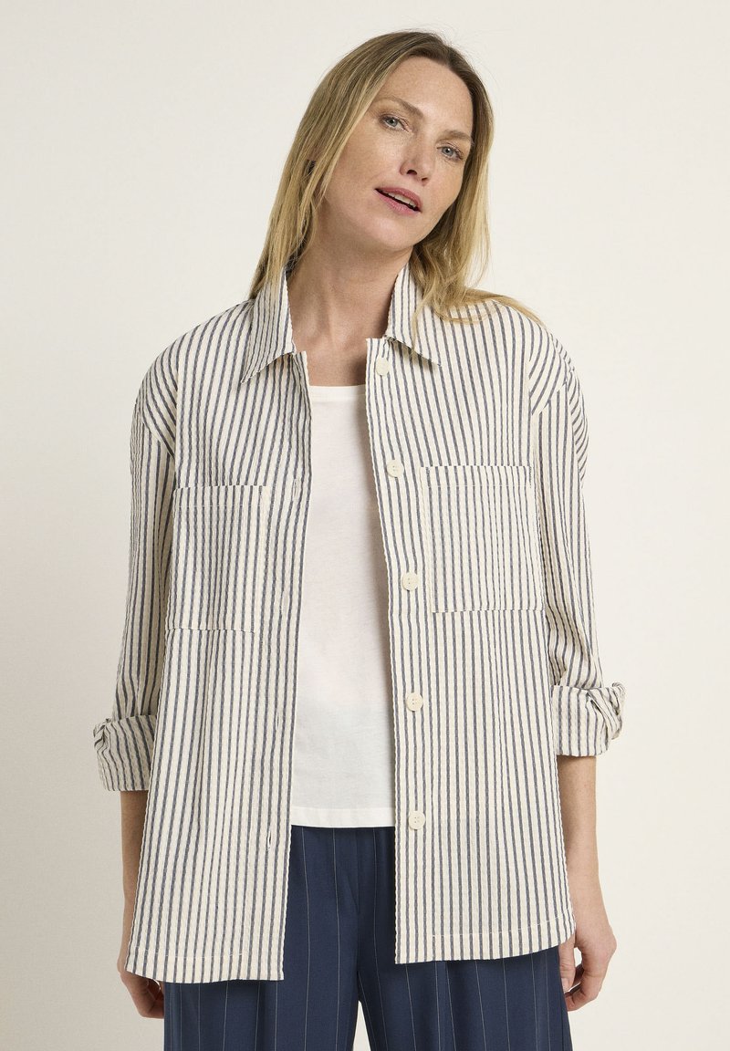 Striped shirt in beige and navy with button closure, two front pockets, and rolled sleeves, made from lightweight fabric.