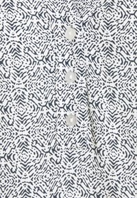 Biała tkanina z czarnym geometrycznym i falistym wzorem, z trzema okrągłymi białymi guzikami na pionowym zapięciu.