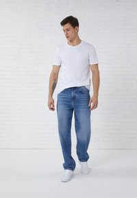 Witte katoenen t-shirt gecombineerd met blauwe denim jeans. De jeans hebben een relaxte pasvorm en zijn licht vervaagd. Schoenen zijn witte sneakers.