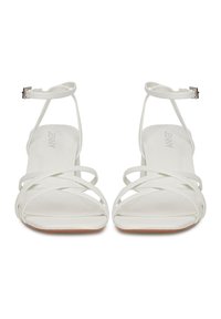 Sandale albe cu toc, cu bretele subțiri încrucișate și cataramă la gleznă. Textură netedă, design cu vârf deschis și talpă plată cu o ușoară înălțare a tocului.