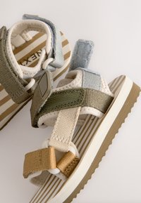 Sandales à brides avec un mélange de tons terre (vert, beige, bleu) et des matériaux texturés, avec un design de semelle rayée. Fermetures Velcro incluses.