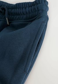 Laivansiniset jogger-housut, jotka on valmistettu pehmeästä kankaasta. Niissä on elastinen vyötärö, nyöri ja sivutaskut, joiden pinta on sileä.