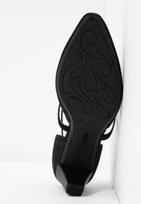 Chaussure à talon haut en daim noir avec un motif de semelle complexe, dotée de brides ajustables et d'un talon effilé pour plus de stabilité.
