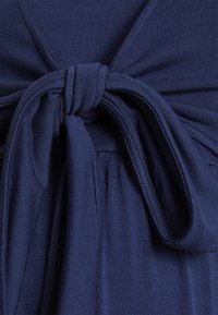 Tecido azul marinho com uma textura suave, apresentando um detalhe de laço torcido na cintura, rodeado por tecido franzido que cria um design fluido.