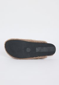 Sole of a brown fuzzy slipper with black ridged non-slip rubber sole, displayed flat against a white background.