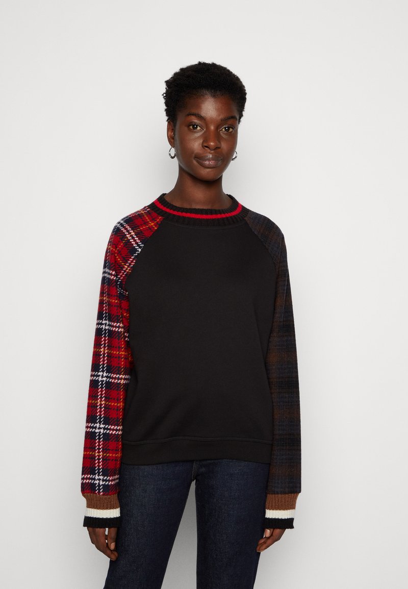 Czarna bluza z dresówki z rękawami z tkaniny w kratę w odcieniach czerwieni i niebieskiego. Posiada ściągacz na dekolcie oraz kontrastowe ściągacze przy mankietach.