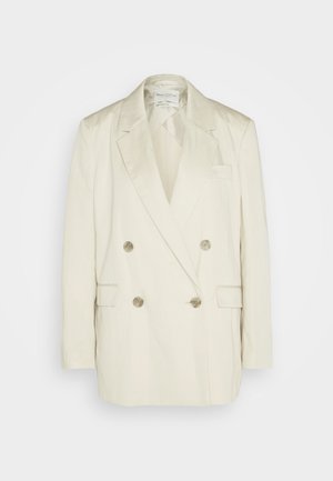 Podwójnie zapięta marynarka z kremowego lnu z szalowymi klapami, dwoma przednimi kieszeniami i metalowymi guzikami. Prosty krój i gładka tekstura.