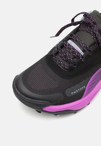 Černá sportovní bota s fialovými akcenty, síťovanou vrstvou, vzorovanými tkaničkami a flexibilní podrážkou. Obsahuje branding a vyztuženou špičku.
