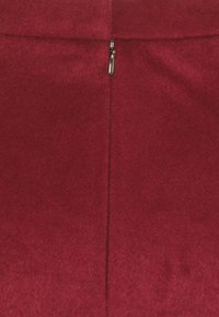 Burgundy ullkjol med en slät yta, en dold dragkedjedetalj bak, och en figurnära design med minimala sömmar.