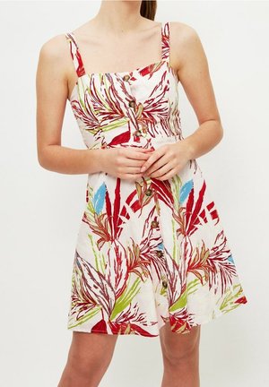 Jurk met bloemenpatroon in wit met rode, groene en blauwe accenten. Voorzien van spaghettibandjes, een getailleerd lijfje en knoopdetails aan de voorkant.