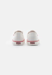 Sneaker bianche in tela con accenti rossi e logo Levi's sul tallone. Design a punta tonda, bassi con una superficie testurizzata.