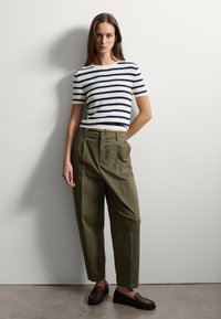 Haut à manches courtes rayé en blanc et bleu marine, associé à un pantalon taille haute vert olive. Chaussures mocassins marron. Design simple et épuré.