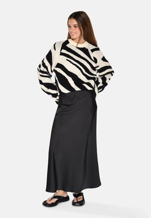 Maglione a righe bianco e nero con fitting largo, abbinato a una lunga gonna nera in satin lucido e sandali piatti neri.