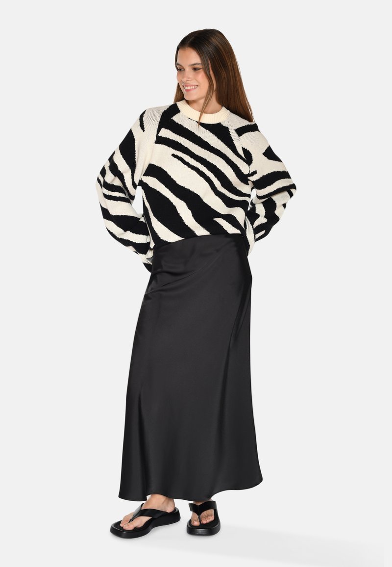 Sort og hvid stribet striktrøje med en løs pasform, sammen med en lang, glat sort satin nederdel og flade sorte sandaler.