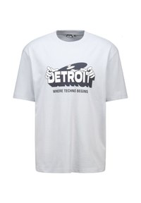 White cotton t-shirt featuring bold black graphic text "DETROIT WHERE TECHNO BEGINS" with stylized hands and a record detail. Short sleeves.