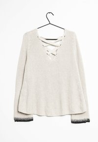 Beige stickad långärmad tröja med korskorsade snören vid V-halsen och svarta gradientärmar, hängande på en svart galge.