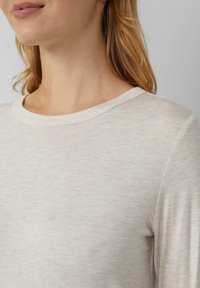 Jasnobeżowa koszula z długim rękawem i okrągłym dekoltem; miękka faktura z delikatnym melanżowym wzorem. Materiał z mieszanki bawełny.