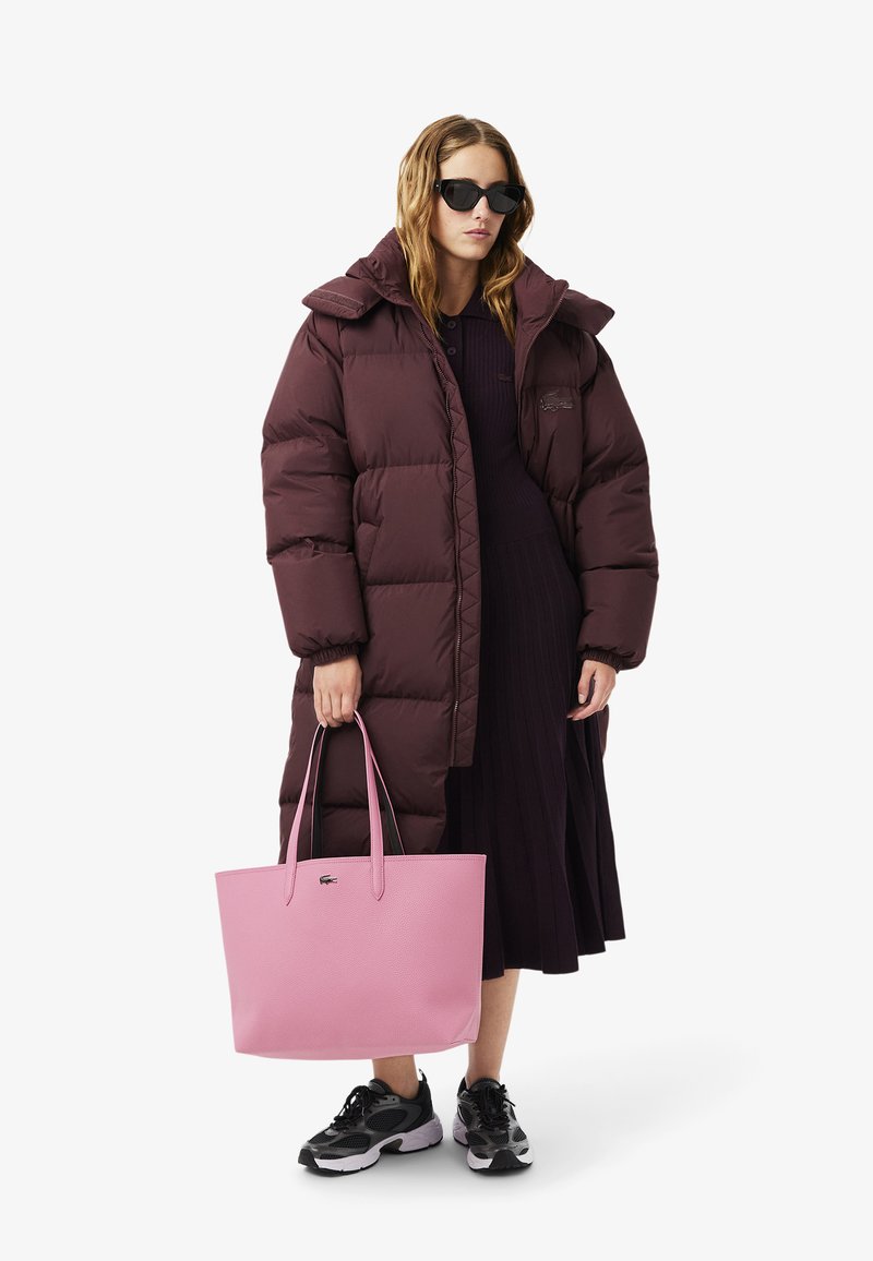 Abrigo tipo puff en burdeos oscuro, bolso de mano rosa, zapatillas negras y gafas de sol. Presenta un gran cuello y un diseño de costura único en el abrigo.