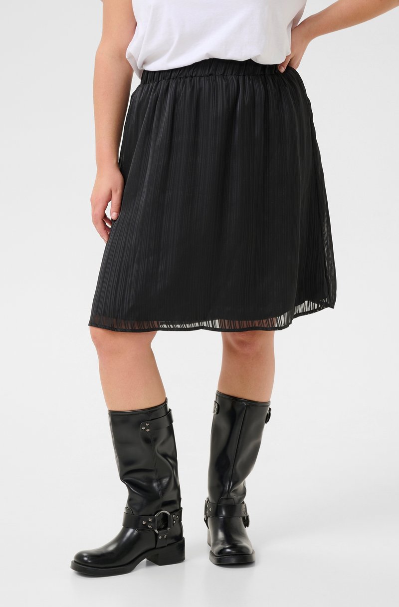 Zwarte geplooide rok met een elastische tailleband, gecombineerd met kniehoge zwarte leren laarzen met gespen en studs.