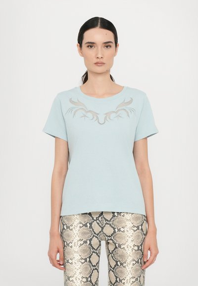 T-shirt bleu clair à manches courtes avec un col rond et un motif graphique décoratif gris sur la poitrine, associé à des leggings ajustés à motif serpent.