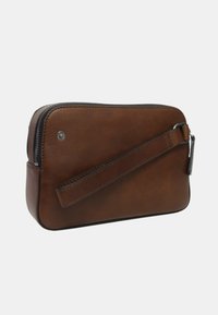 Pochette da polso in pelle marrone con chiusura a zip e strap attaccata su sfondo bianco semplice.
