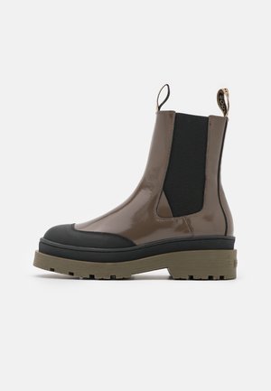 Bottes courtes en cuir verni marron avec des accents en caoutchouc noir et une semelle épaisse. Présentent des panneaux latéraux élastiques et une languette de tirage pour un enfilement facile.