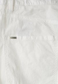 Tissu blanc en gros plan montrant une poche arrière avec une petite étiquette métallique de marque indiquant "Street One" sur la ceinture cousue.