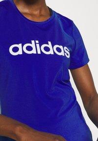 Blue athletic t-shirt featuring a prominent white "adidas" logo. Smooth texture, round neckline, and short sleeves.