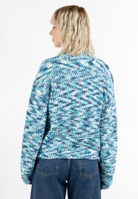 Kék és fehér kötött pulóver, laza szabással, texturált mintával és cropped hosszal. A hátulról nézve széles ujjak és bordázott alsó szegély látható.