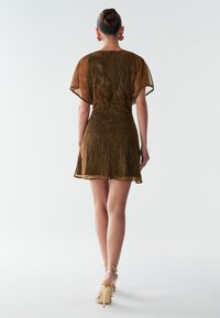 Kort brun kjole med løs pasform, tekstureret stof, korte ærmer og en flared kant. Bæres med gyldne hæle sandaler.