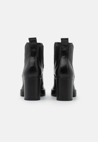 Stivaletti alla caviglia in pelle nera con finitura lucida, caratterizzati da un tacco a blocco e linguette per facilitare la calzata, con dettagli cuciti lungo i lati.