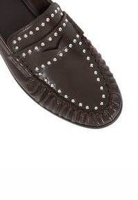 Brown leather loafers featuring studded detail, a rounded toe, and a ruffled accent along the edge. Smooth texture with stitching visible.
