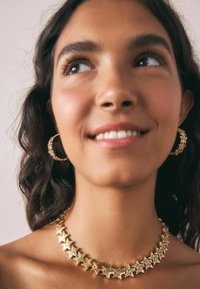 Kulla tähekujuline kaelakee ja sobivad rõngas kõrvarõngad, mõlemad sujuvate ja sädeleva aktsendiga, kantud palja naha vastas.