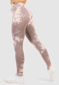 Hooggetailleerde legging in beige met een tie-dye patroon, gemaakt van soepel, rekbaar materiaal en een aansluitend ontwerp. Een lichte glans is zichtbaar.
