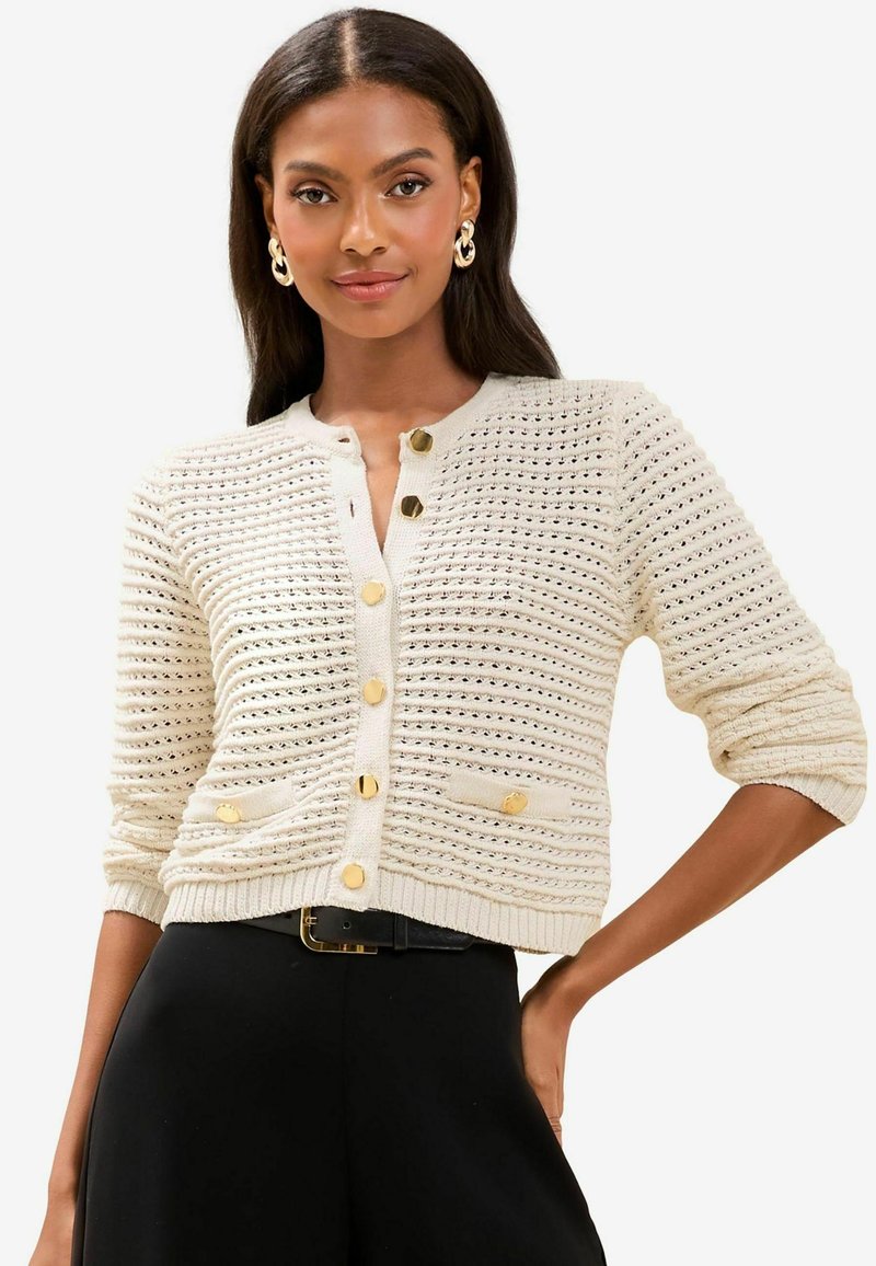 Cardigan lavorato a maglia in beige con un design testurizzato, bottoni dorati e due tasche anteriori, con maniche a tre quarti e scollo rotondo.