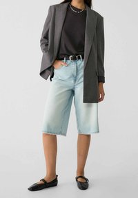 Blazer grande de rayas grises, camiseta negra, bermudas de mezclilla azul claro, cinturón negro y bailarinas negras con detalle de lazo.