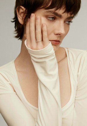 Blusa de manga larga en color crema con una tela suave y elástica. Presenta un escote profundo y un detalle recortado en el hombro.