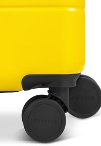 Geel harde koffer met een textuurafwerking; voorzien van zwarte plastic wielen met "ETERNITIVE" branding en een gebogen zwart accent aan de onderkant.