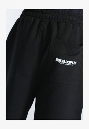 Schwarze Jogginghose mit elastischem Bund und einer Seitentasche. Mit einem weißen gestickten Logo "MULTIPLY" in der Nähe der Tasche.