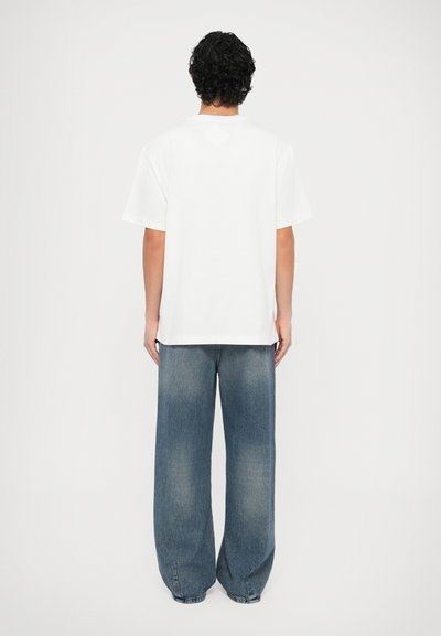 Άσπρο βαμβακερό μπλουζάκι με κοντά μανίκια και άνετη εφαρμογή, σε συνδυασμό με ανοιχτόχρωμα τζιν παντελόνια φαρδύ πόδι με ξεθωριασμένες λεπτομέρειες.