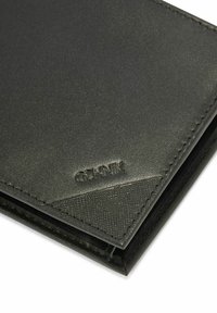 Czarny skórzany portfel o teksturowanej powierzchni, z trójkątnym akcentem wzorniczym i wytłoczonym logo na przedniej stronie. Widoczne metalowe elementy.