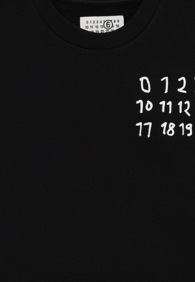 Czarny bawełniany t-shirt z okrągłym dekoltem, z białymi haftowanymi cyframi oraz metką z rozmiarem i instrukcjami prania.