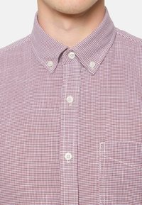 Camisa de botones en patrón de cuadros rojos y blancos, material de algodón, con cuello estándar, un bolsillo en el pecho y botones redondos.