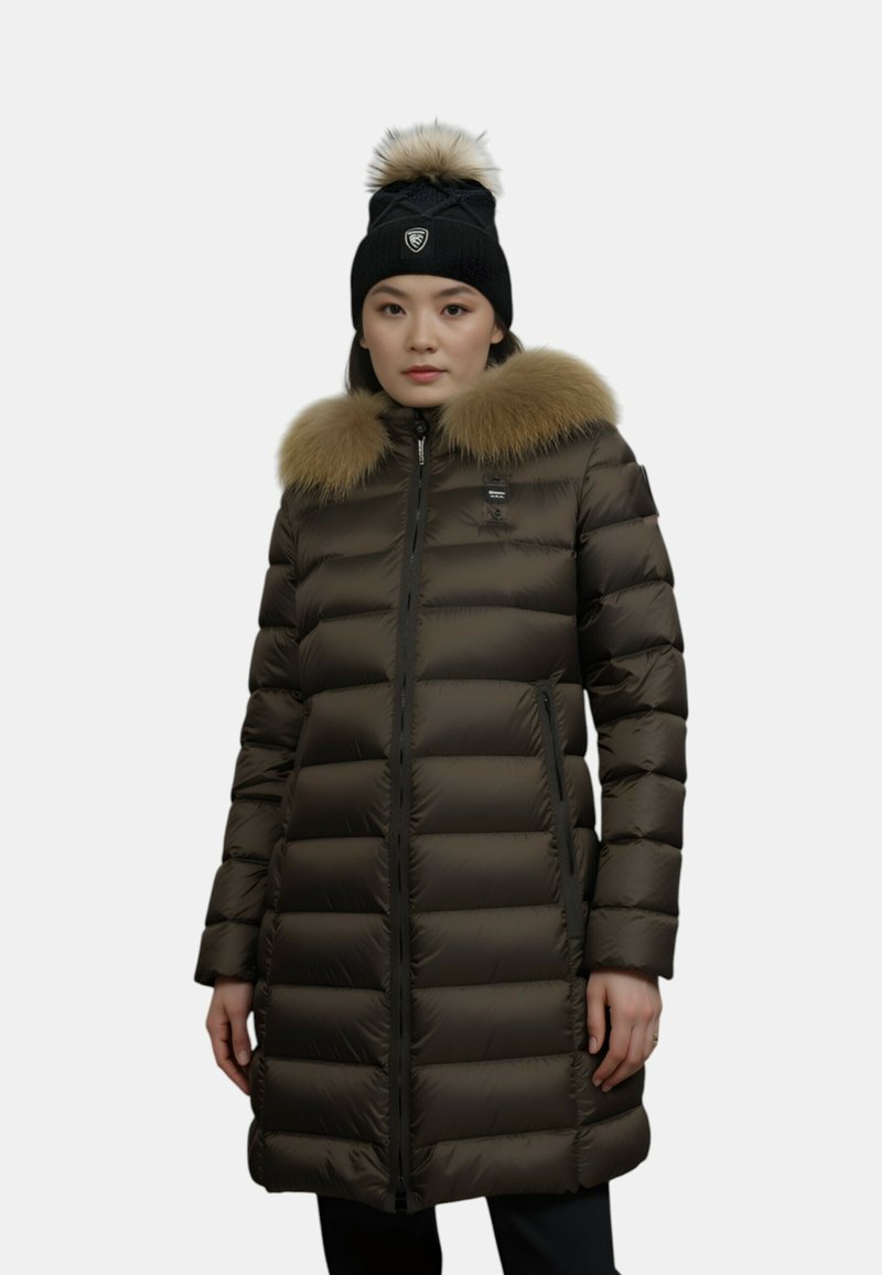 Parka marrone con motivo a righe orizzontali e cappuccio foderato in pelliccia, abbinata a un berretto lavorato a maglia nero con pompon e logo.