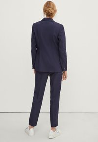 Blazer blu navy e pantaloni sartoriali realizzati in tessuto morbido, con un classico rever e un design elegante. Indossati con scarpe da ginnastica bianche per un contrasto.