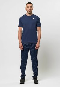 Marineblauwe sportshirt met korte mouwen en logo op de borst, gecombineerd met bijpassende marineblauwe broek met een glanzende textuur.
