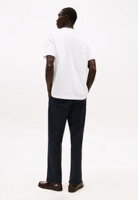 Hvit bomulls t-skjorte med korte ermer, kombinert med marineblå vide bukser. Antrekket fullføres med mørkebrune sko.