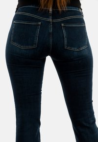 Jeans de mezclilla azul oscuro con un diseño ajustado, que presentan dos bolsillos traseros con un patrón de costura distintivo y acentos de costura dorada.